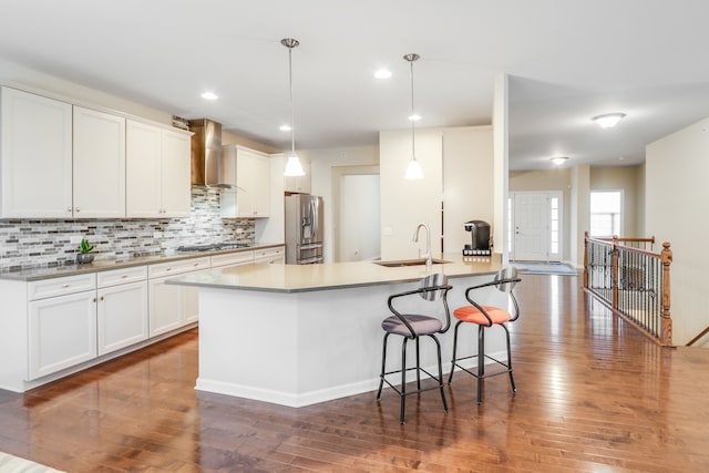 kitchen with wall chimney exhaust hood, hanging light fixtures, white cabinetry, appliances with stainless steel finishes, and sink