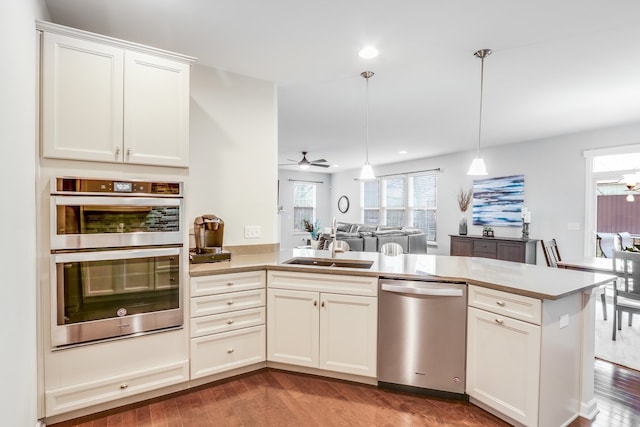 kitchen with kitchen peninsula, pendant lighting, appliances with stainless steel finishes, ceiling fan, and sink