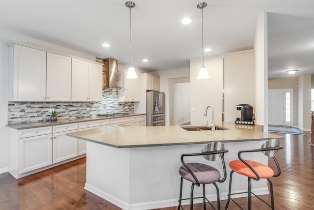 kitchen featuring sink, white cabinetry, hanging light fixtures, wall chimney range hood, and appliances with stainless steel finishes