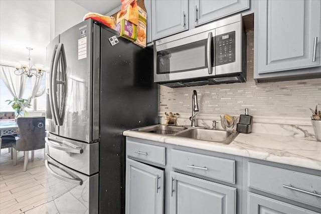 kitchen featuring decorative backsplash, appliances with stainless steel finishes, sink, a notable chandelier, and gray cabinets