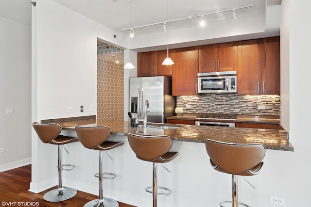 kitchen with sink, hanging light fixtures, a kitchen breakfast bar, backsplash, and appliances with stainless steel finishes