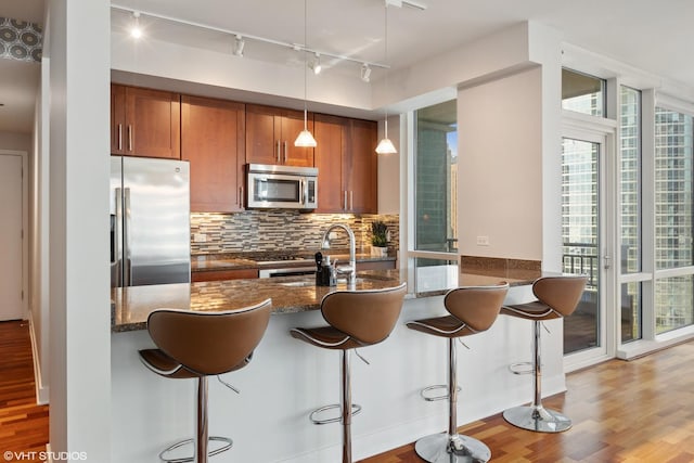 kitchen with tasteful backsplash, dark stone counters, decorative light fixtures, a breakfast bar area, and appliances with stainless steel finishes