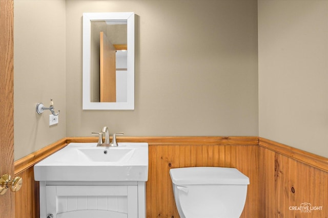 bathroom featuring vanity, wood walls, and toilet