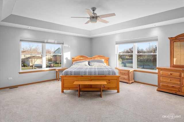 carpeted bedroom with a tray ceiling, multiple windows, and ceiling fan