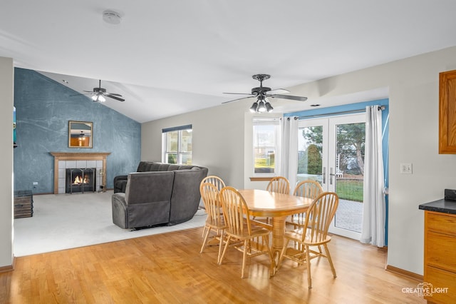 dining room featuring light hardwood / wood-style floors, a tiled fireplace, french doors, and vaulted ceiling