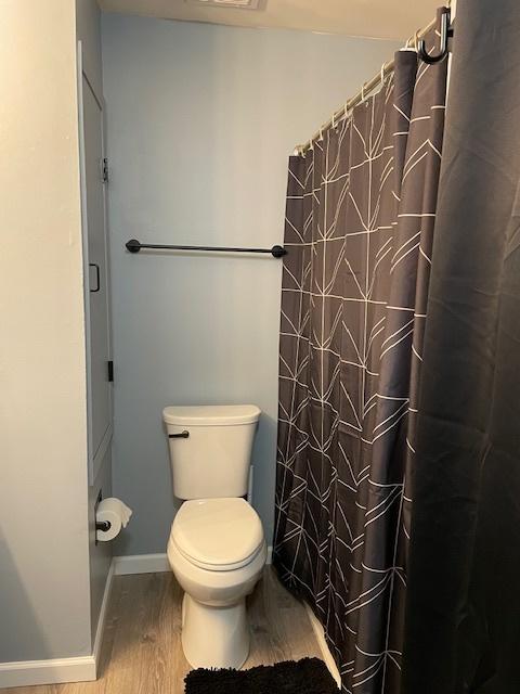 bathroom with hardwood / wood-style flooring, toilet, and a shower with shower curtain