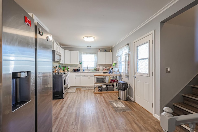 kitchen featuring backsplash, appliances with stainless steel finishes, light wood-type flooring, white cabinets, and ornamental molding