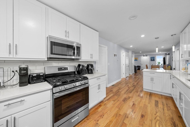 kitchen featuring decorative backsplash, appliances with stainless steel finishes, pendant lighting, light hardwood / wood-style floors, and white cabinetry