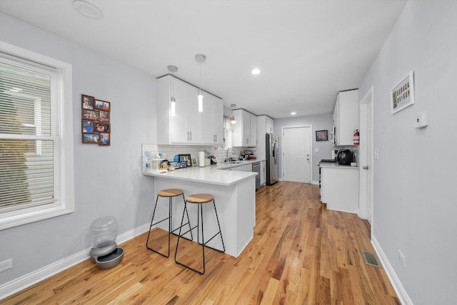 kitchen with sink, kitchen peninsula, light wood-type flooring, decorative light fixtures, and white cabinetry