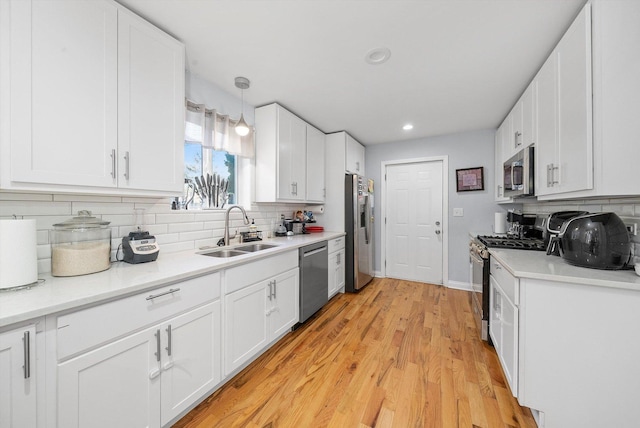 kitchen featuring white cabinetry, sink, hanging light fixtures, stainless steel appliances, and light hardwood / wood-style flooring