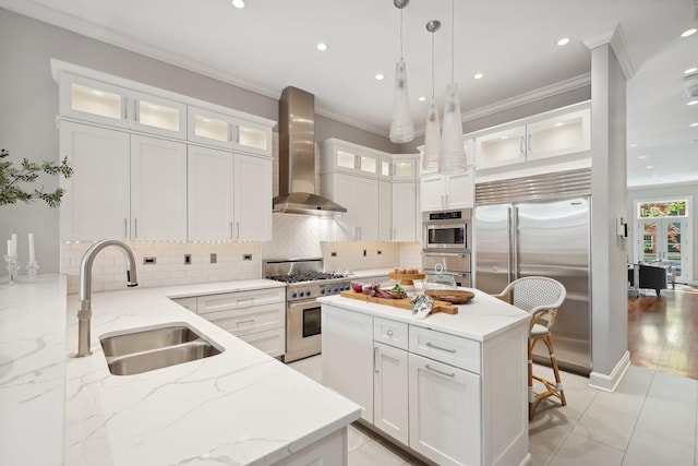 kitchen with wall chimney exhaust hood, sink, pendant lighting, high quality appliances, and white cabinetry