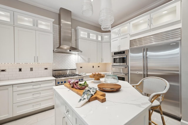 kitchen featuring white cabinets, wall chimney range hood, light tile patterned floors, a kitchen bar, and stainless steel appliances