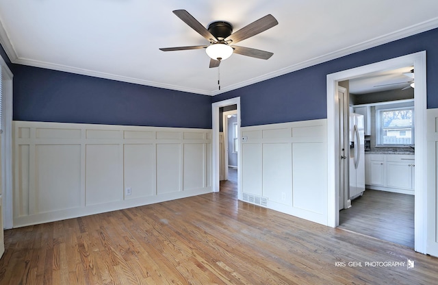 unfurnished bedroom with white refrigerator with ice dispenser, crown molding, ensuite bath, light hardwood / wood-style flooring, and ceiling fan