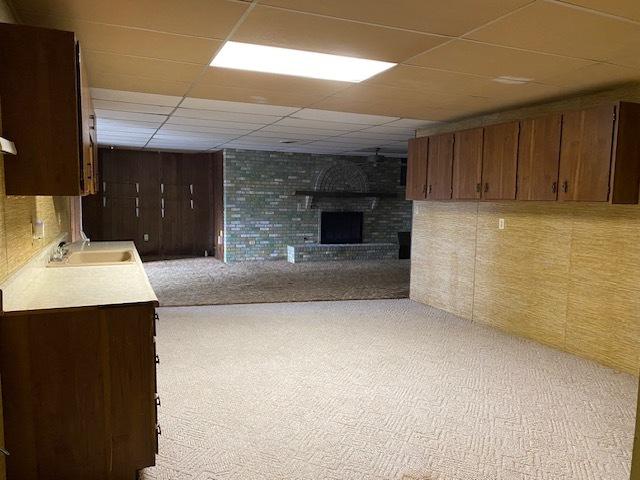 interior space featuring a drop ceiling, a fireplace, light colored carpet, and sink