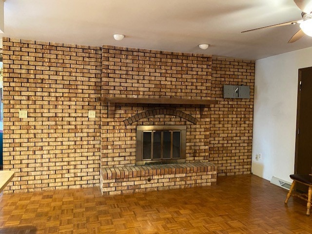 unfurnished living room featuring parquet flooring, ceiling fan, a fireplace, and brick wall