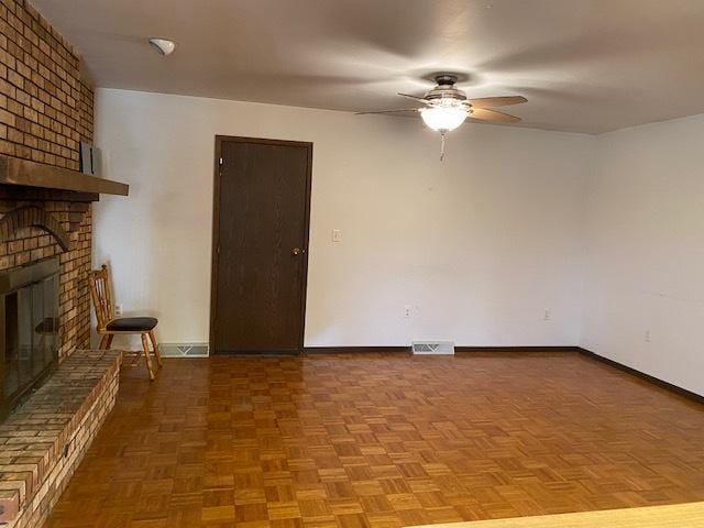 unfurnished living room featuring parquet flooring, a brick fireplace, and ceiling fan