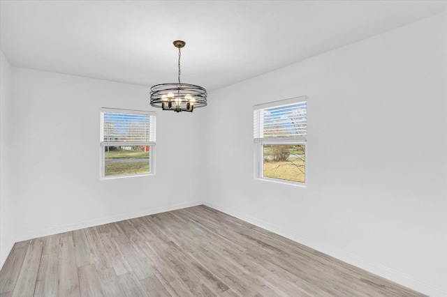 spare room with a notable chandelier and light wood-type flooring