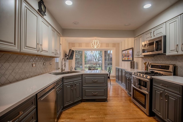 kitchen featuring backsplash, hanging light fixtures, sink, appliances with stainless steel finishes, and light hardwood / wood-style floors