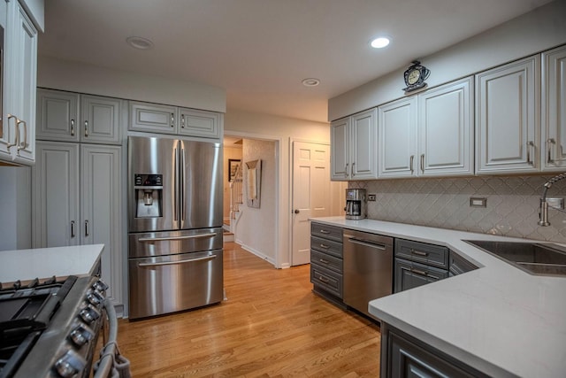 kitchen with sink, light hardwood / wood-style flooring, decorative backsplash, gray cabinets, and stainless steel appliances