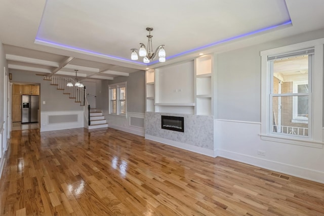 unfurnished living room featuring coffered ceiling, built in shelves, wood-type flooring, beam ceiling, and a chandelier