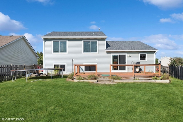 rear view of property featuring a lawn, a deck, and a trampoline