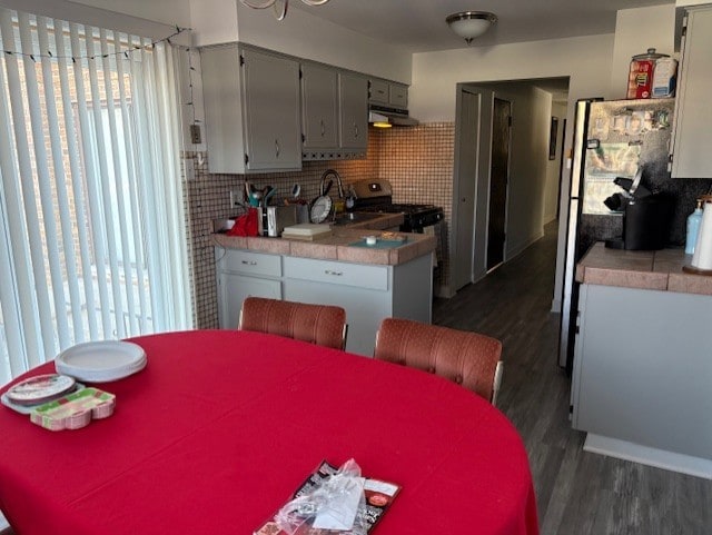 kitchen featuring tile counters, sink, dark wood-type flooring, tasteful backsplash, and stainless steel range oven