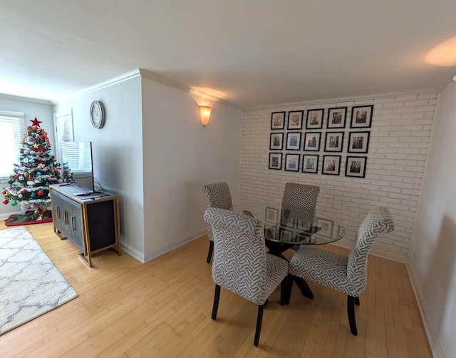 dining area with crown molding, brick wall, and light wood-type flooring