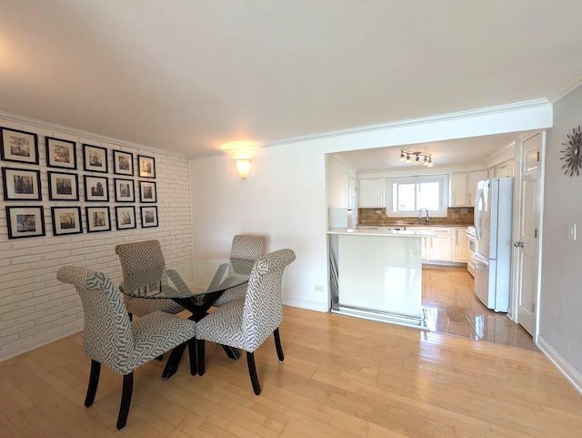 dining space featuring sink, light wood-type flooring, ornamental molding, and brick wall