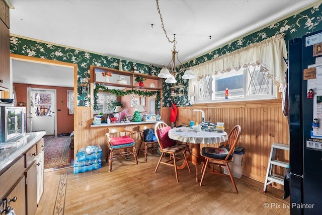 dining area with a chandelier, light wood-type flooring, and wooden walls