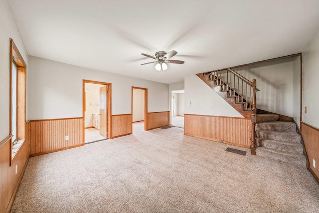 unfurnished living room with wood walls, ceiling fan, and light colored carpet