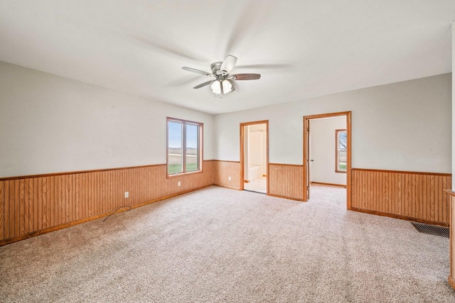 unfurnished bedroom with wooden walls, ceiling fan, and light carpet