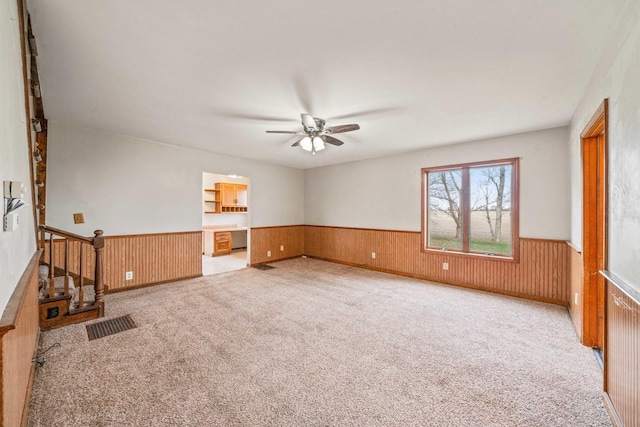 unfurnished living room featuring light carpet, ceiling fan, and wooden walls