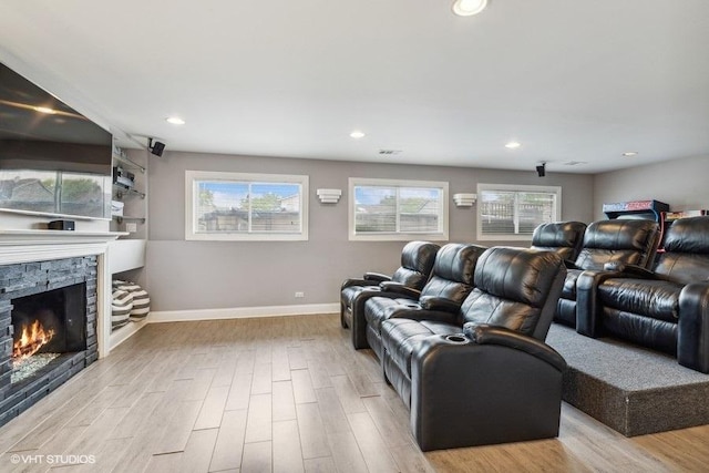 cinema room with wood finished floors, baseboards, a stone fireplace, and recessed lighting