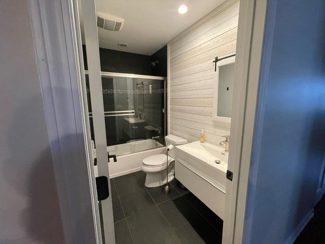 full bath with vanity, tile patterned flooring, toilet, wood walls, and bath / shower combo with glass door