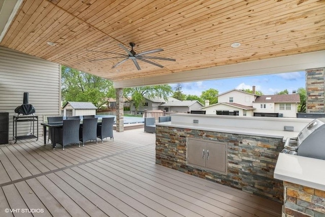wooden terrace featuring area for grilling, an outbuilding, ceiling fan, a storage shed, and outdoor dining space