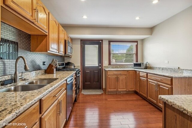 kitchen featuring a sink, dark wood-style flooring, appliances with stainless steel finishes, decorative backsplash, and light stone counters