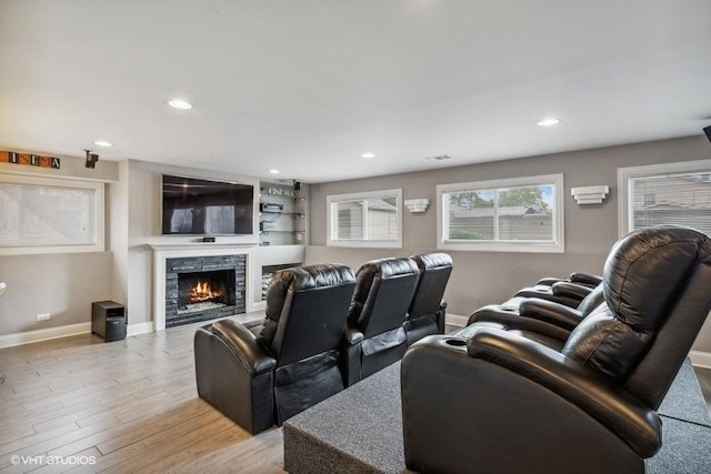 home theater featuring a warm lit fireplace, baseboards, light wood-type flooring, and recessed lighting