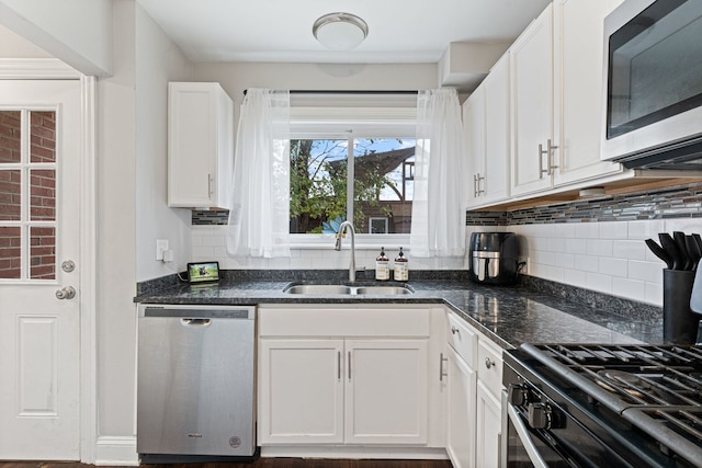 kitchen with white cabinetry, sink, backsplash, dark stone countertops, and appliances with stainless steel finishes