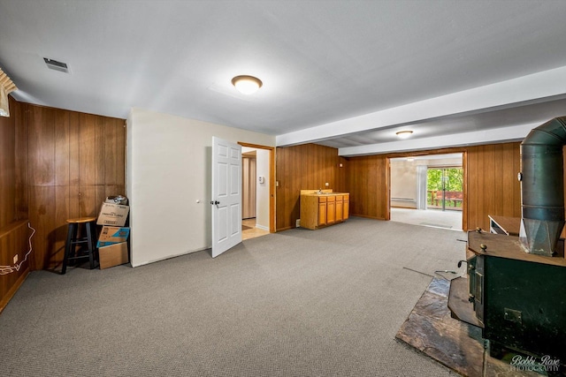 interior space with a wood stove, wooden walls, baseboard heating, beamed ceiling, and carpet floors