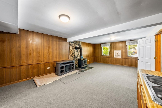 interior space with a wood stove, wood walls, sink, and light colored carpet