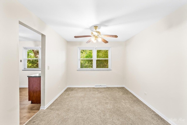 unfurnished room featuring ceiling fan, light carpet, and a wealth of natural light