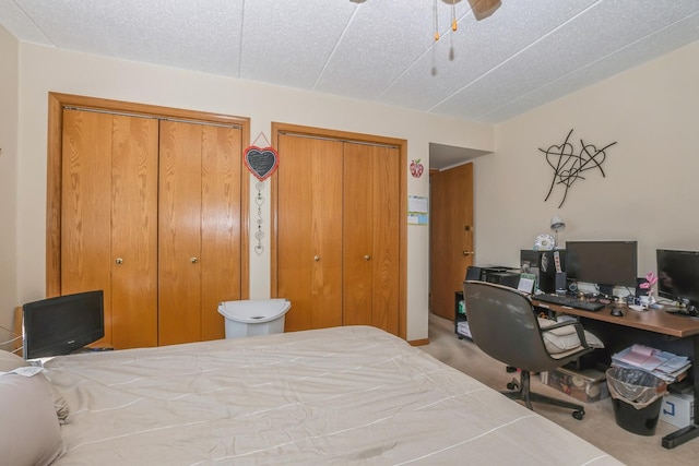 carpeted bedroom with a textured ceiling, ceiling fan, and two closets