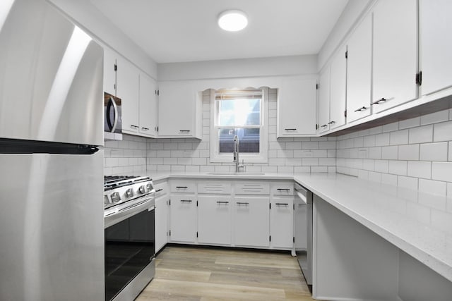 kitchen with tasteful backsplash, stainless steel appliances, sink, white cabinets, and light hardwood / wood-style floors