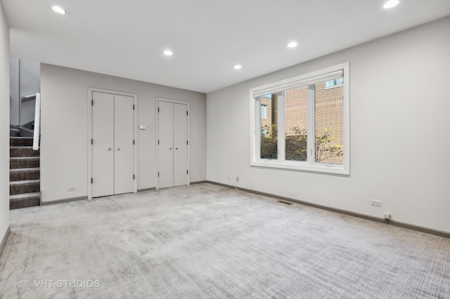 unfurnished bedroom with two closets and light colored carpet