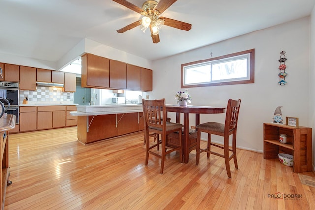 kitchen with ceiling fan, backsplash, double oven, and light hardwood / wood-style floors