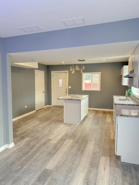 kitchen featuring white cabinetry, a center island, sink, hanging light fixtures, and light hardwood / wood-style floors