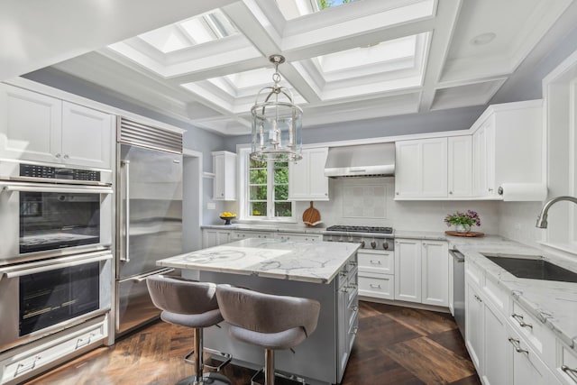 kitchen featuring stainless steel appliances, sink, wall chimney range hood, a center island, and white cabinetry