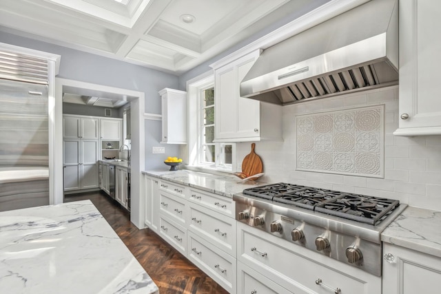 kitchen with light stone countertops, appliances with stainless steel finishes, wall chimney exhaust hood, coffered ceiling, and white cabinetry