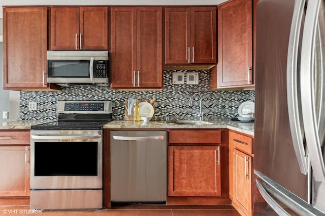 kitchen with tasteful backsplash, appliances with stainless steel finishes, light stone counters, and a sink