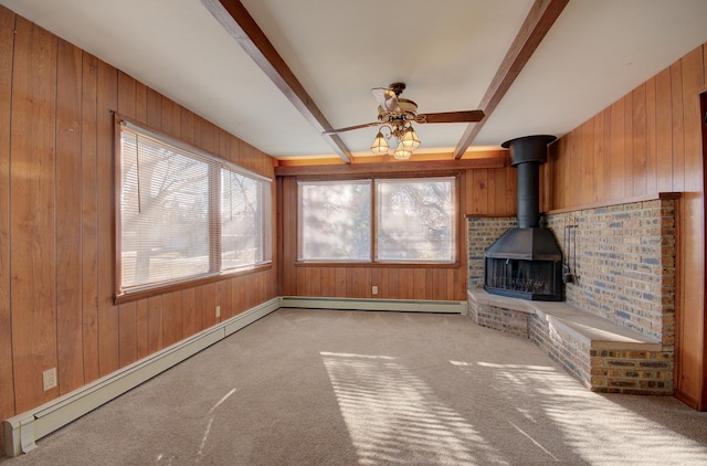 unfurnished living room with beam ceiling, a wood stove, ceiling fan, light carpet, and wooden walls